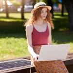 young student female smiling in park with laptop sitting on bench