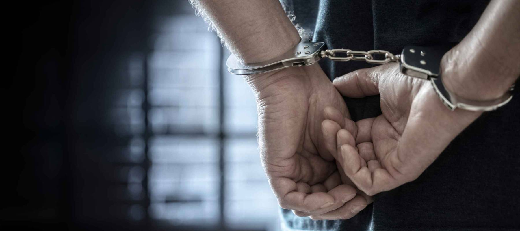 Arrested man in handcuffs with handcuffed hands behind back in prison