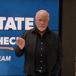 Dave Ramsey speaks in front of a large screen on a television set.
