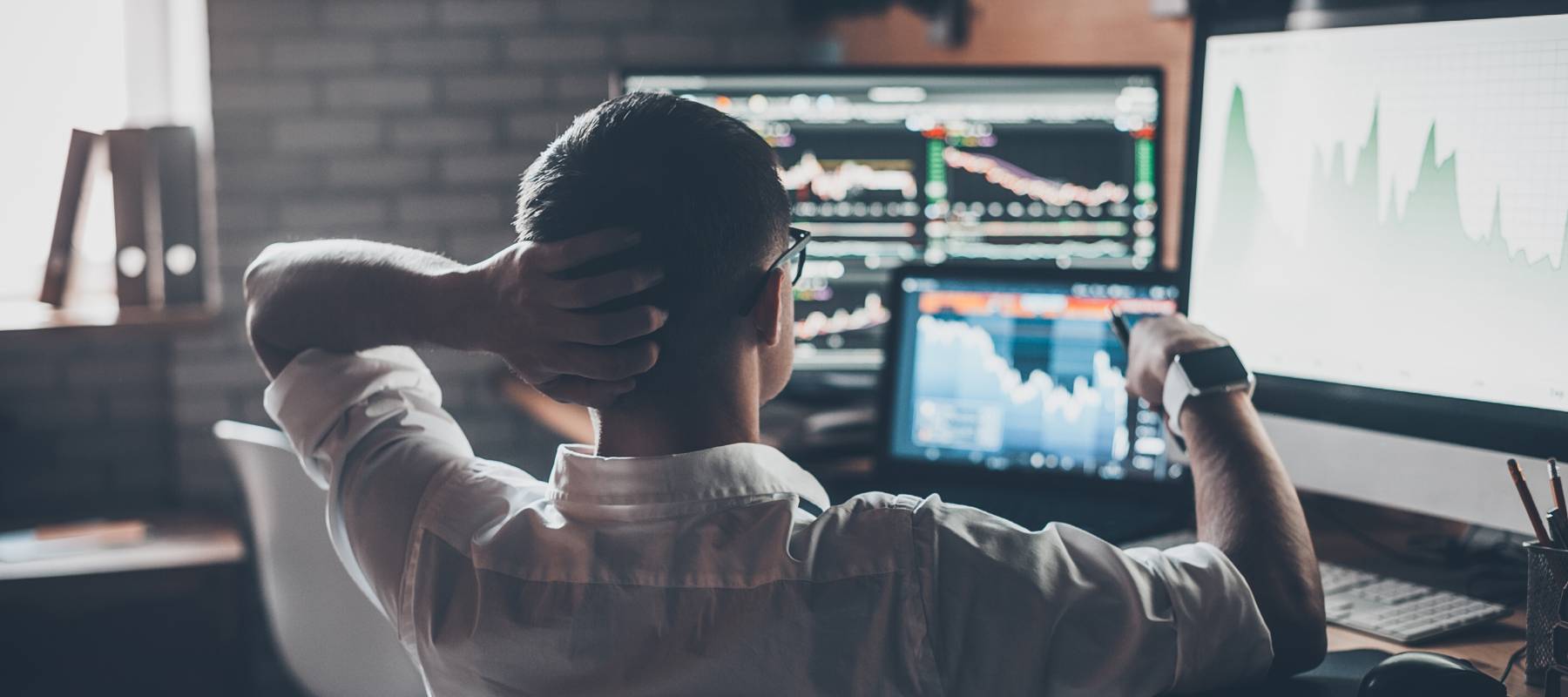 Developing new approaches. Rear view of young man in casual wear holding hand on the back of the head and working while sitting at the desk in creative office