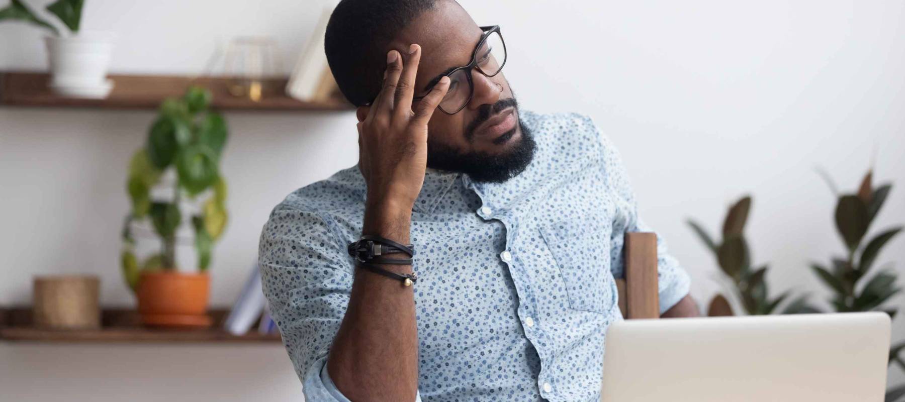 Serious african millennial businessman thinking, searching problem solution sitting alone on chair at modern office desk looking away
