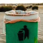 Green waste container on sandy beach. Plastic waste pollution and greenwashing.
