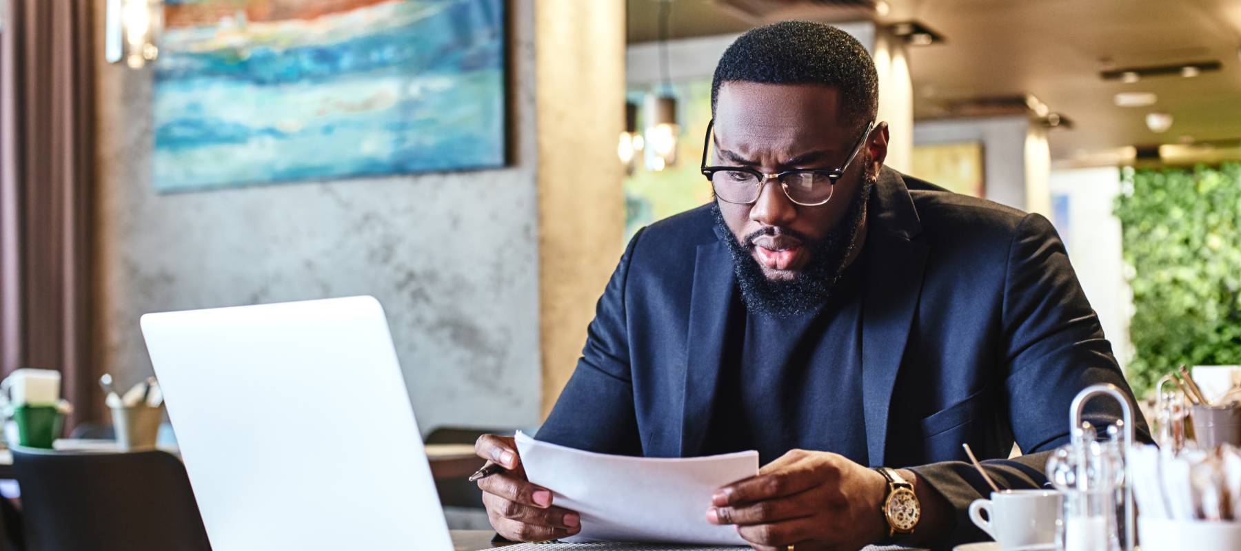 Portrait of dark-skinned businessman in dark-blue jacket and glasses sitting at the table