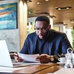 Portrait of dark-skinned businessman in dark-blue jacket and glasses sitting at the table