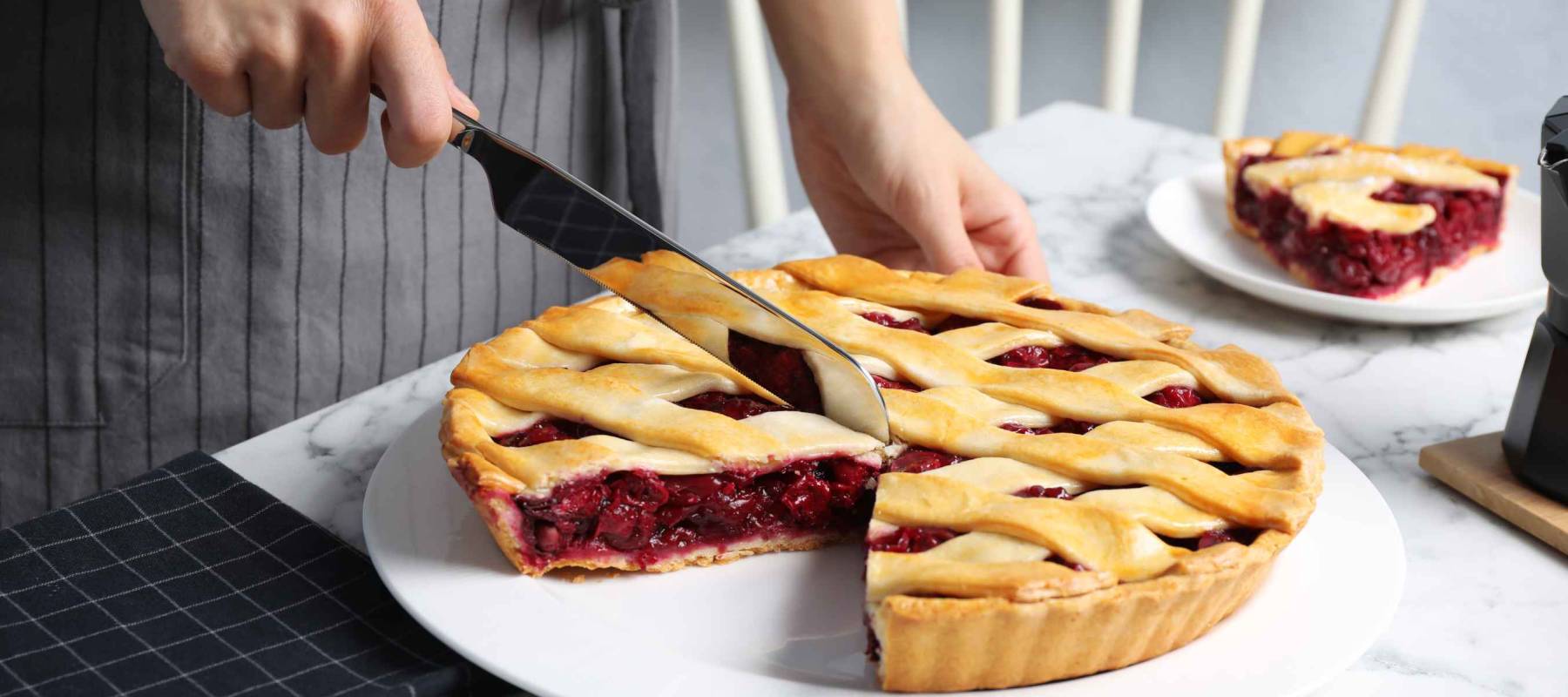 Woman cutting tasty cherry pie at white marble table, closeup