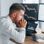 Risky job. Young businessman in formal clothes is in office with multiple screens.