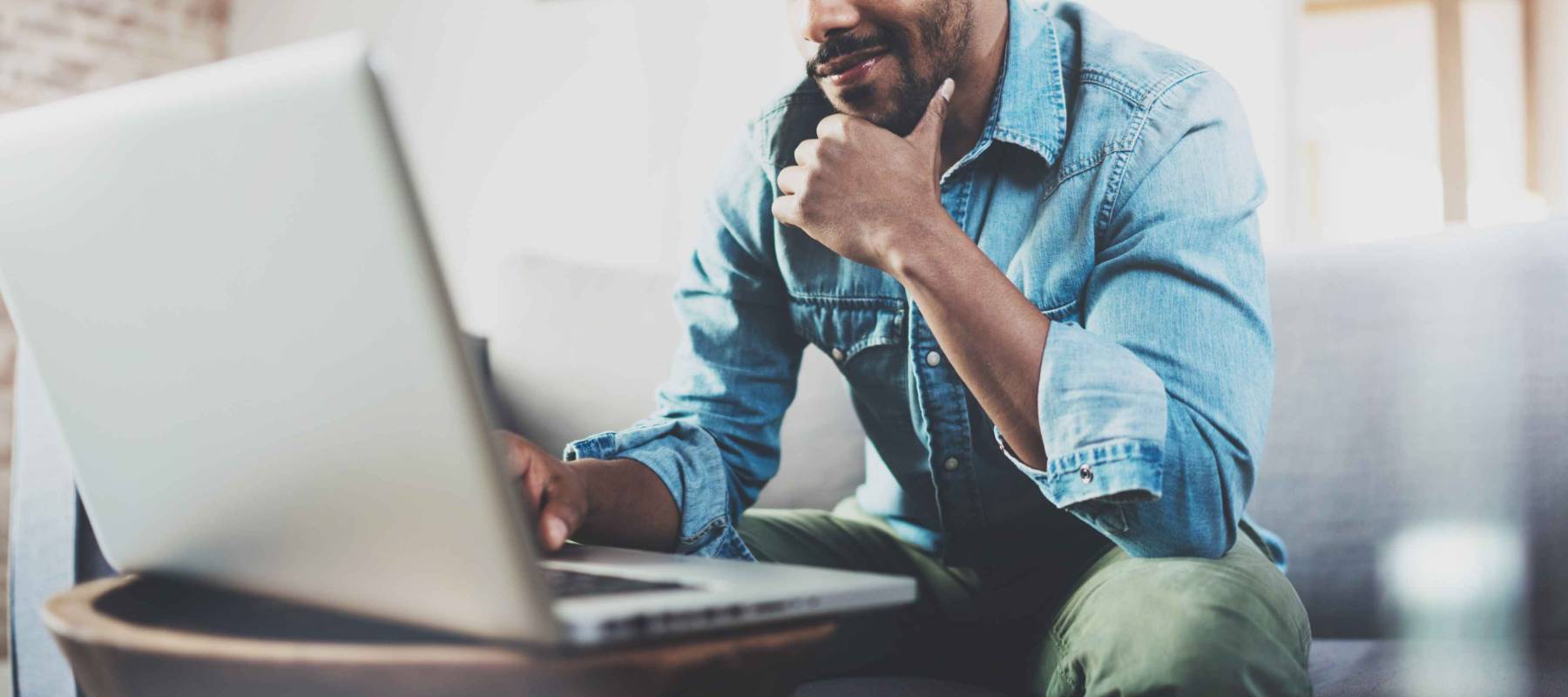 Smiling bearded African man working at home while sitting on the sofa.Concept of young people using mobile devices.Blurred background.Cropped