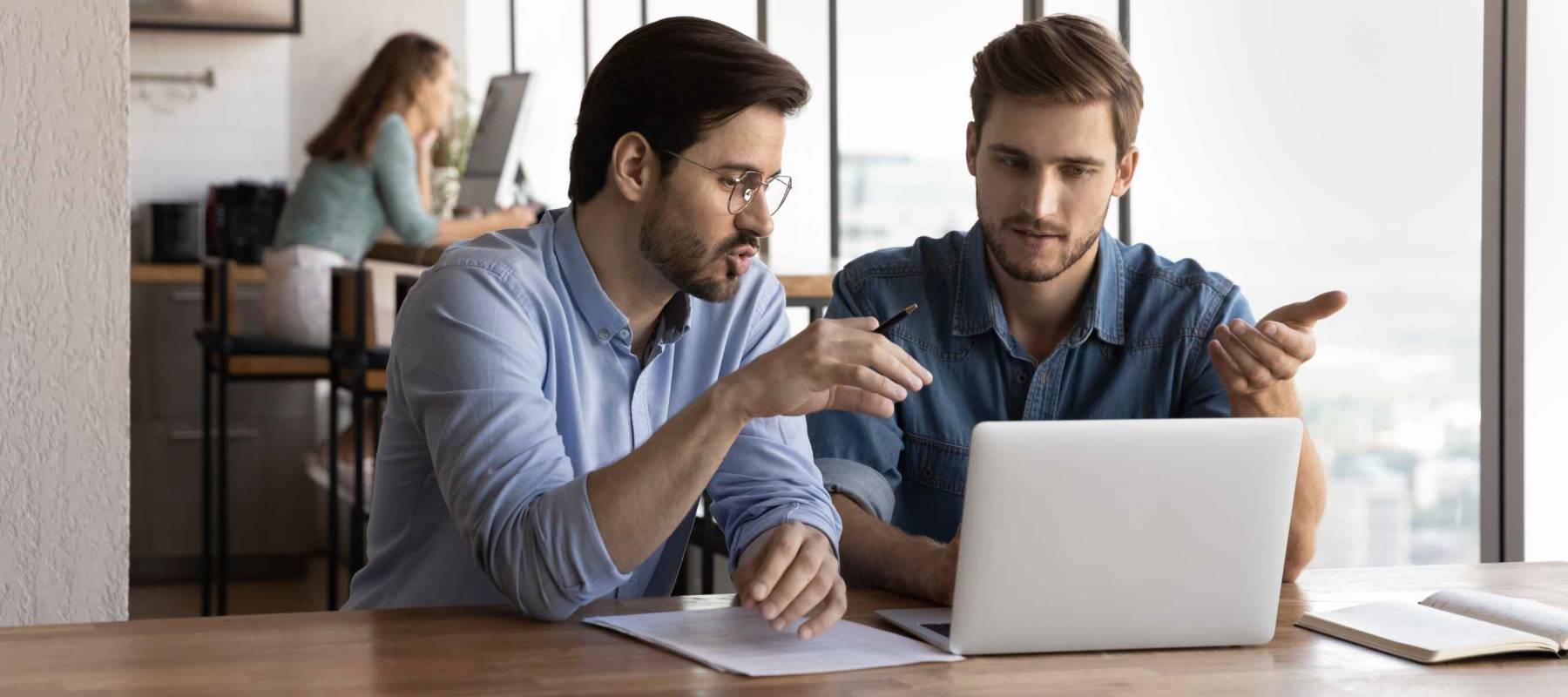 Office employees discussing project at laptop, sharing ideas.