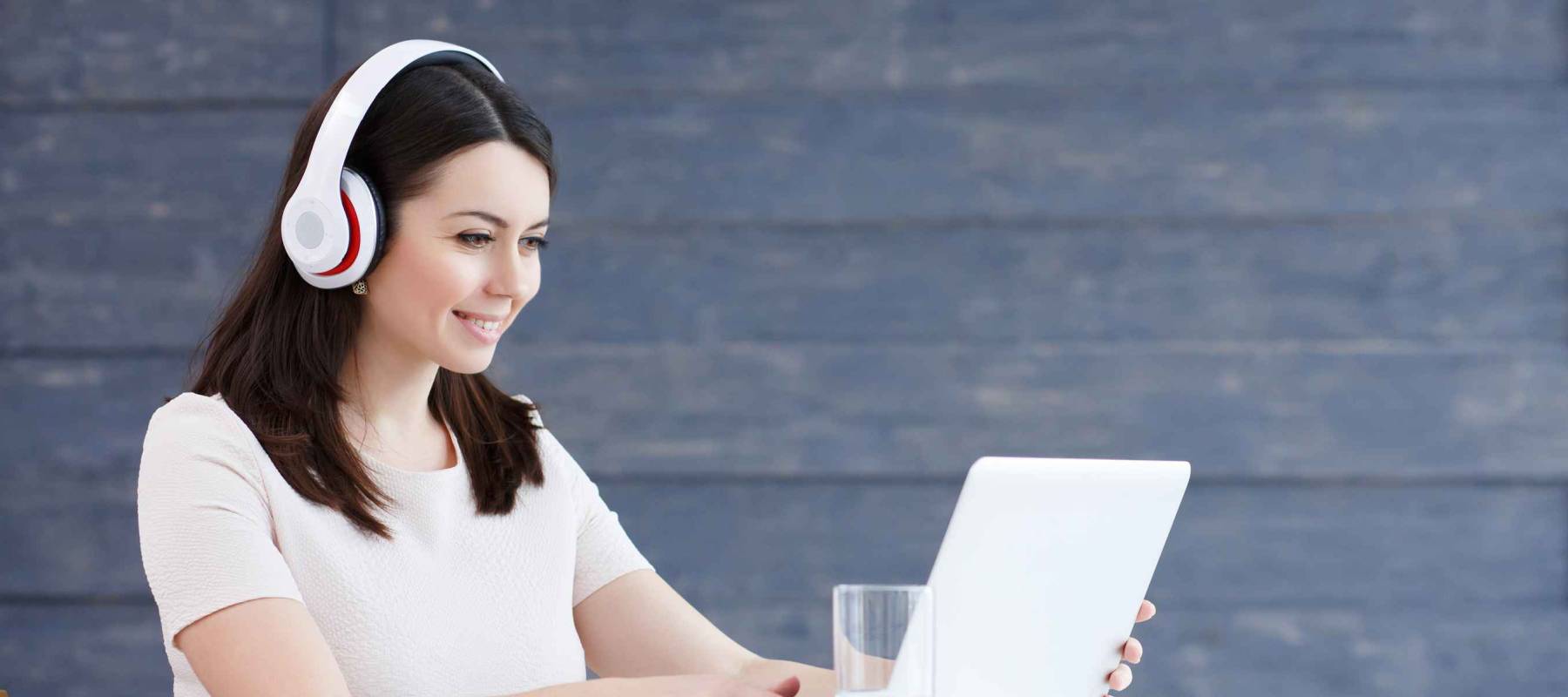 Portrait of a student or young business woman learning on line with headphones and laptop, taking notes in a notebook sitting at desk