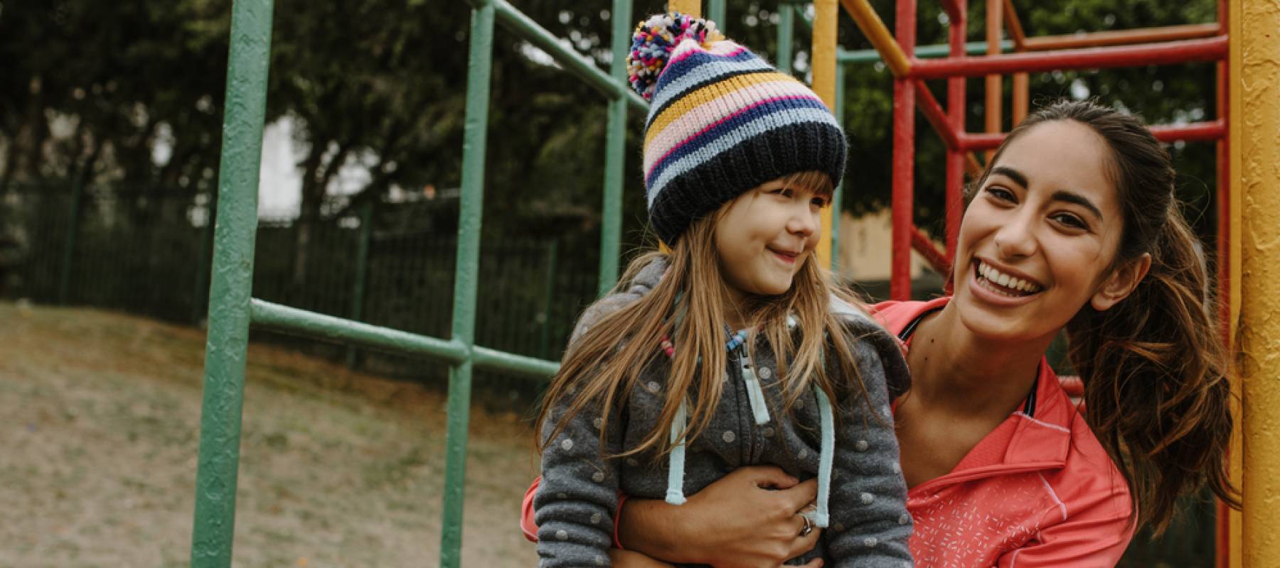 Woman spending time with a girl at the playground, both smiling and laughing.