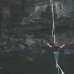 person on a tightrope or slack line perfectly balancing between two cliffs taking a risk for a reward