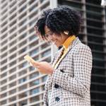 Close-up of african american businesswoman checking her mobile phone while walking to work at financial city district. Business concept.