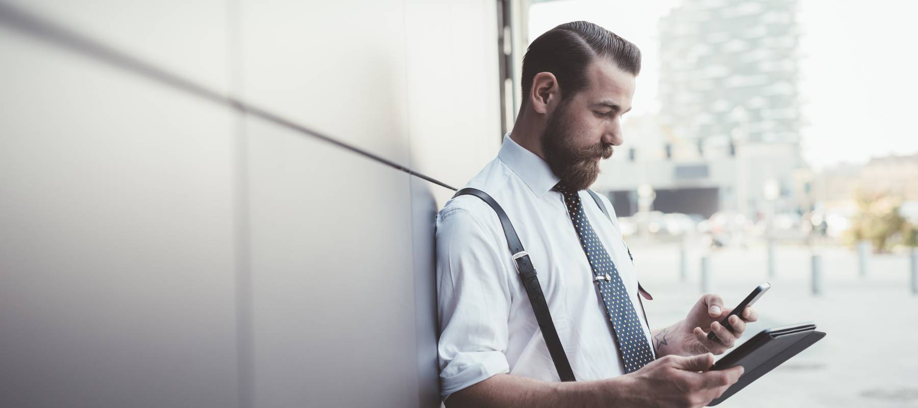 Stylish businessman using smartphone and digital tablet outside office