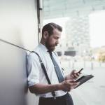 Stylish businessman using smartphone and digital tablet outside office