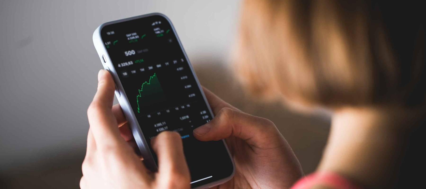 Stock market investor young woman holding a phone investment app index growth chart