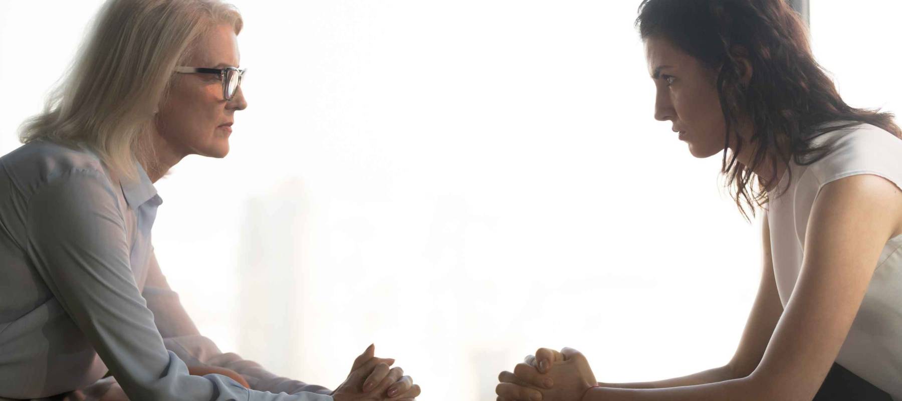 young vs. old business women sitting across from each other, staring with clasped hands ready to battle