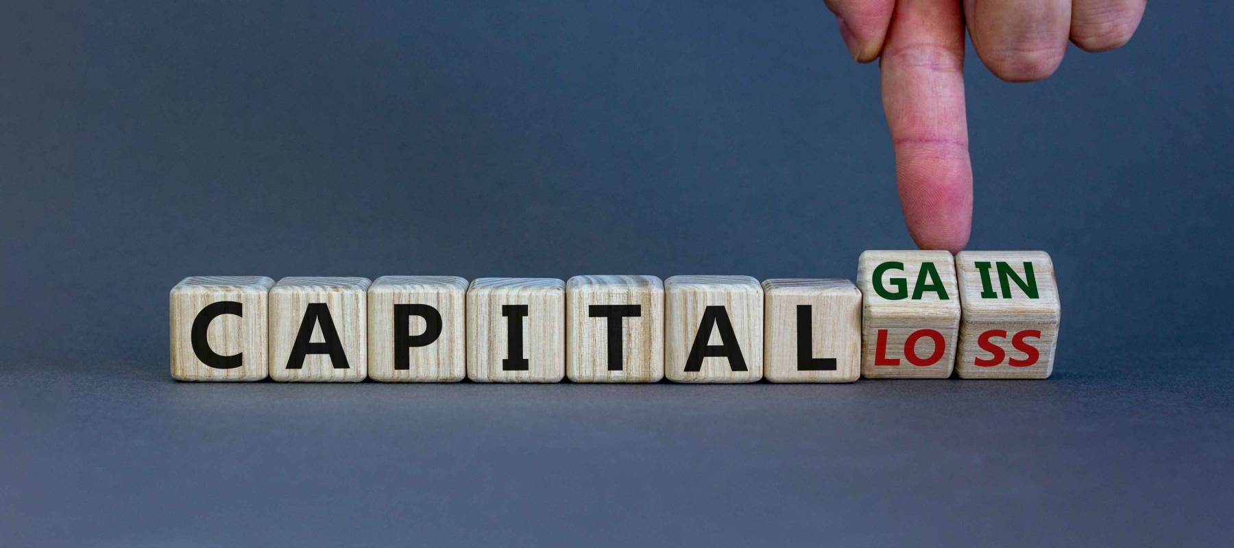 Capital loss or gain symbol. Male hand turns cubes and changes words 'capital loss' to 'capital gain'. Beautiful grey background. Business and capital loss or gain concept. Copy space.