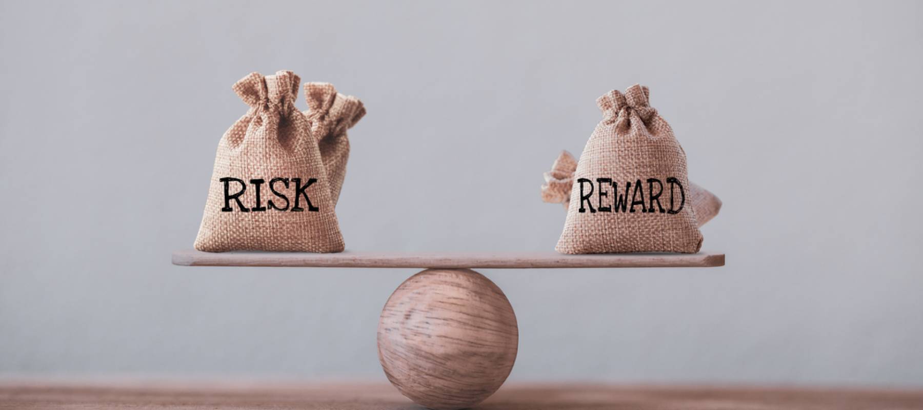 Risk and reward bags on a basic balance scale in equal position on wood table.