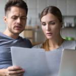 Serious confused couple checking high domestic bills with papers and laptop