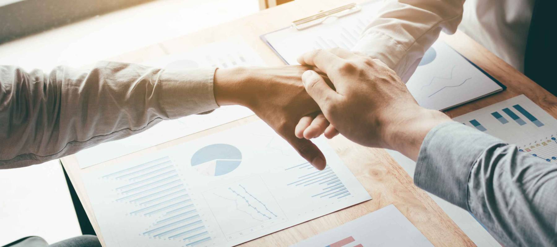 Asian business teamwork with merge hand for success project and chart report on desk.