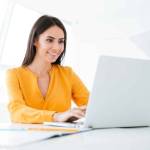 Business woman in orange shirt using laptop computer and sitting by the table in office