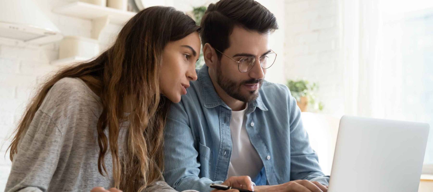 Focused young couple calculating bills, discussing planning budget together, serious wife and husband looking at laptop screen, using online banking services and calculator, checking finances