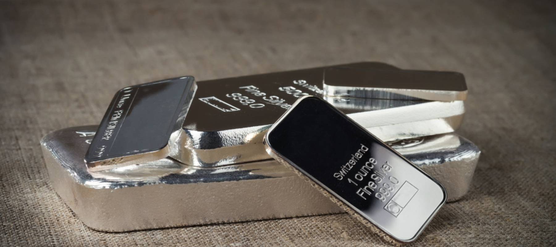 Several silver bars of various weights on a textile texture background.