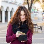 young shopper woman taking out money from wallet on street