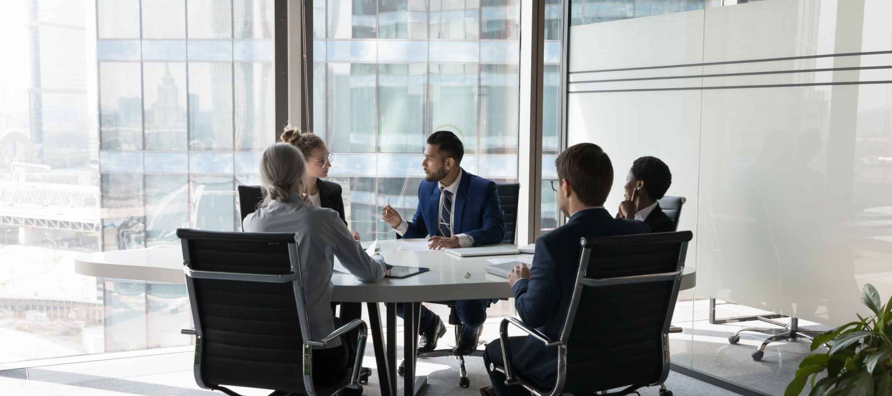 Serious team of professionals, five multi ethnic business people negotiating in modern boardroom, discuss project, consider contract