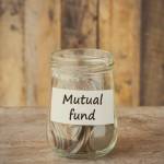 Coins in glass money jar with mutual fund label, financial concept. Vintage wooden background
