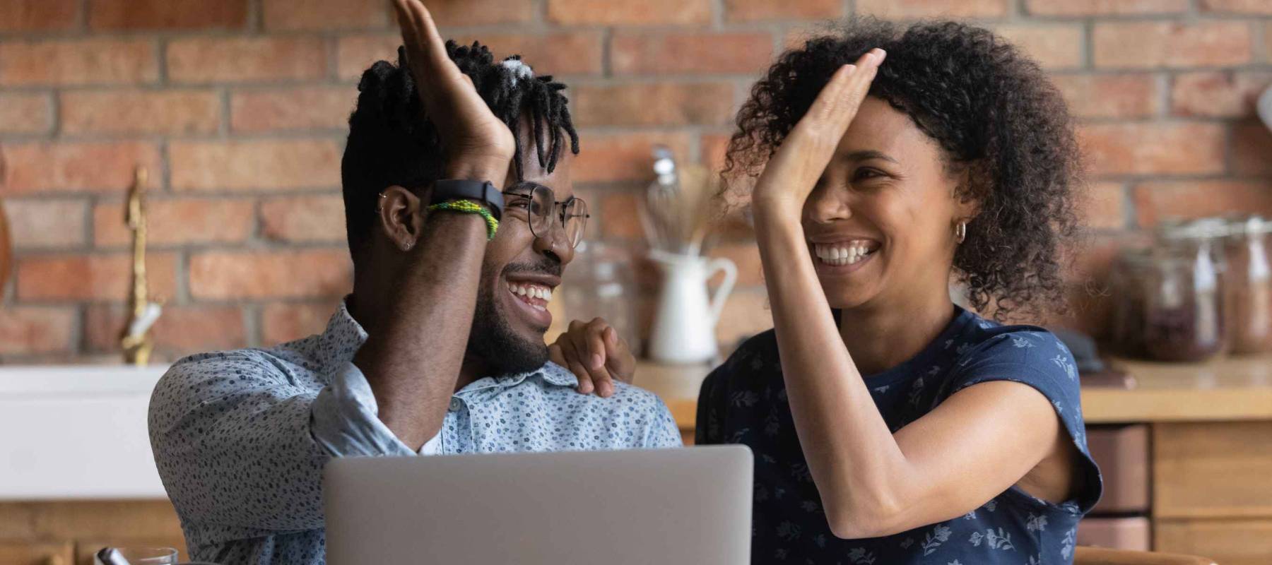 Happy excited Black mixed race couple celebrating financial success at laptop,