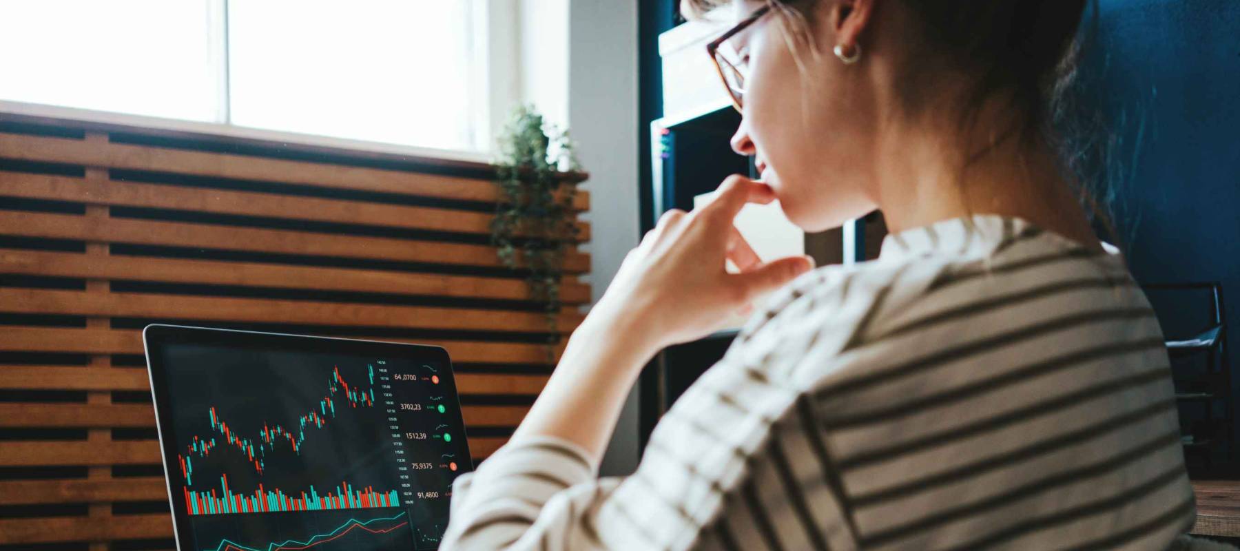 Woman investing in world stock market, using her laptop and online trading soft from home
