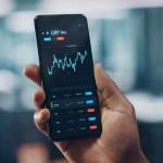Black Businessman Holding Smartphone and Checking Stock and Cryptocurrency Market in Office. African-American Businessperson using Internet with Mobile Phone Device. Over Shoulder Shot