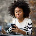 Portrait young african american woman sitting with laptop and using mobile phone