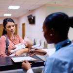 Mom holding baby while talking to receptionist at a doctor's office.