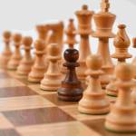 white chess pieces on a board lined up but one dark chess pawn stands among them as different from the rest