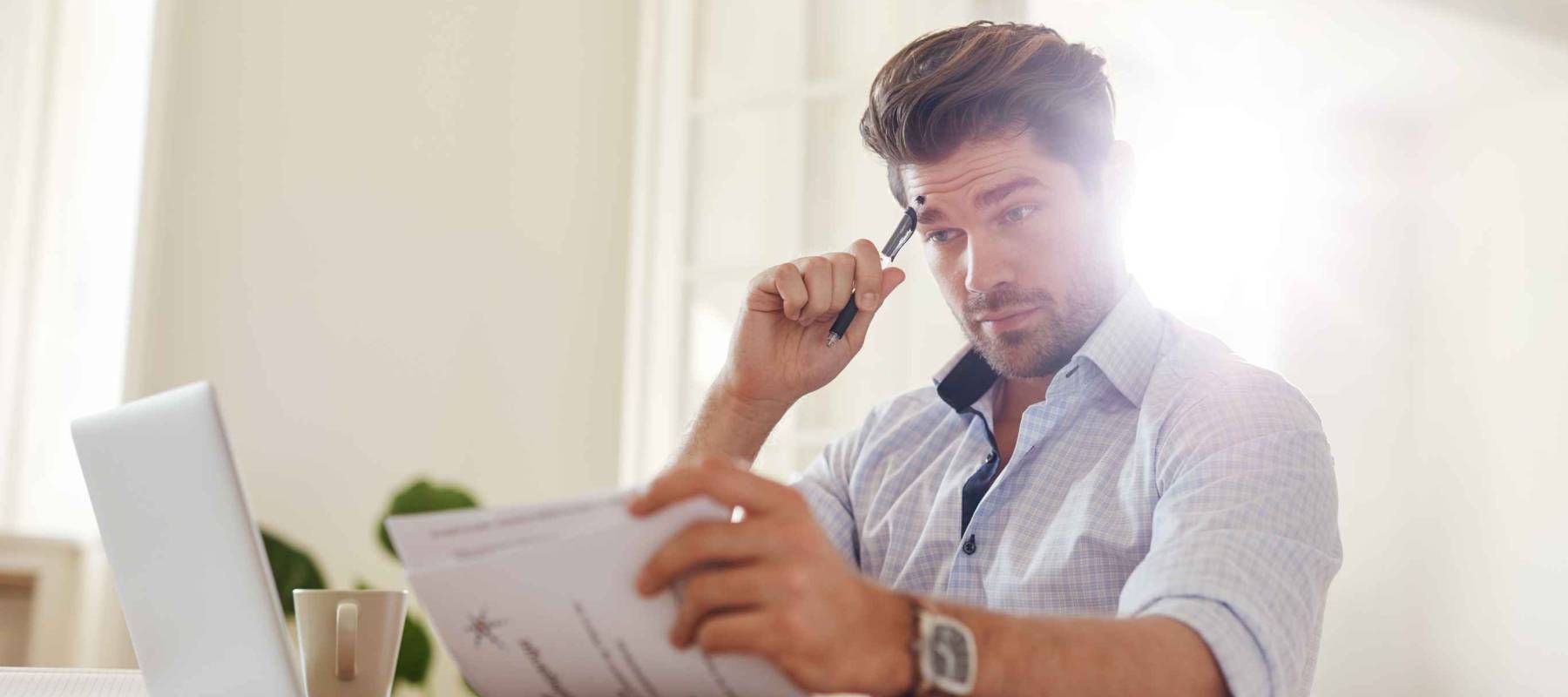 Shot of a young man sitting at table looking at documents and thinking. Business man going through paperwork at home office.