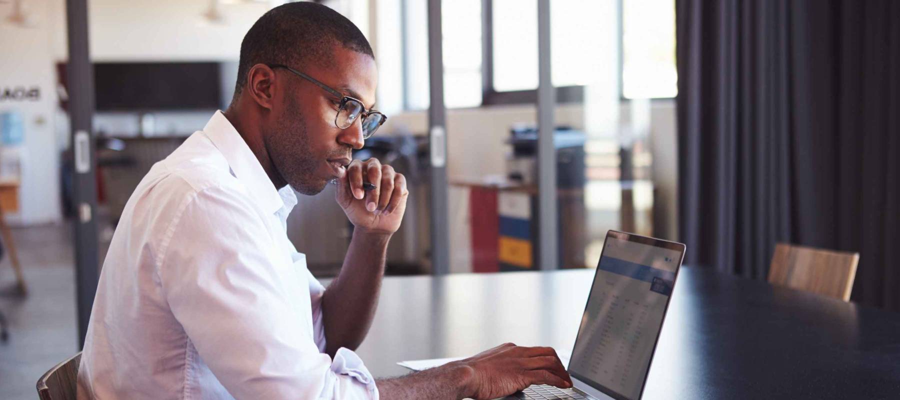 Young black man in wearing glasses using laptop in office