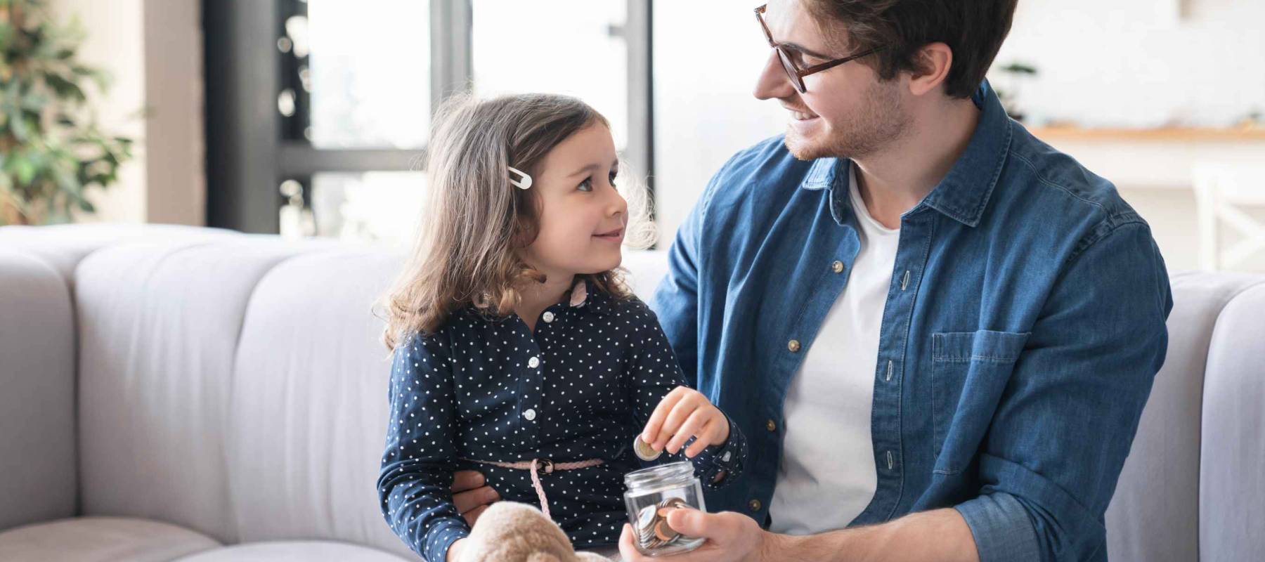 Small girl daughter and her young father putting money to the moneybox piggy bank. Personal Savings. Saving money concept.