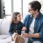 Small girl daughter and her young father putting money to the moneybox piggy bank. Personal Savings. Saving money concept.