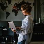 Beautiful young concentrated business woman wearing shirt using laptop while standing in modern workspace