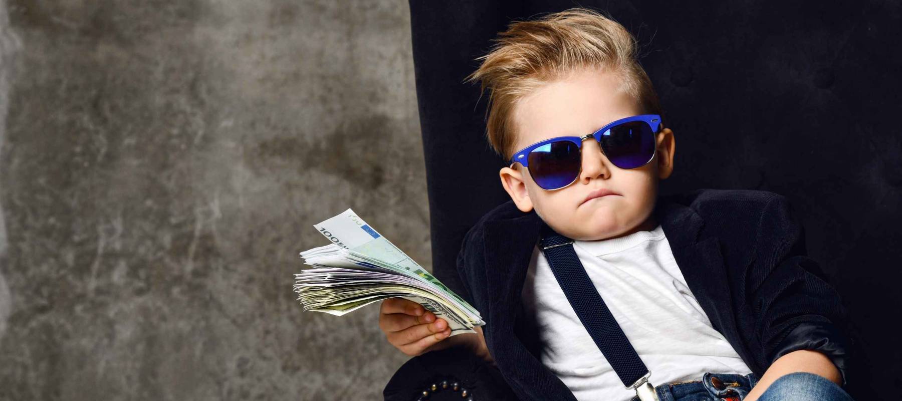 Happy and shoutting arrogant rich kid boy millionaire sits with a bundle of money dollars cash in big luxury armchair holding was of cash.