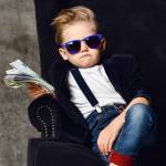 Happy and shoutting arrogant rich kid boy millionaire sits with a bundle of money dollars cash in big luxury armchair holding was of cash.