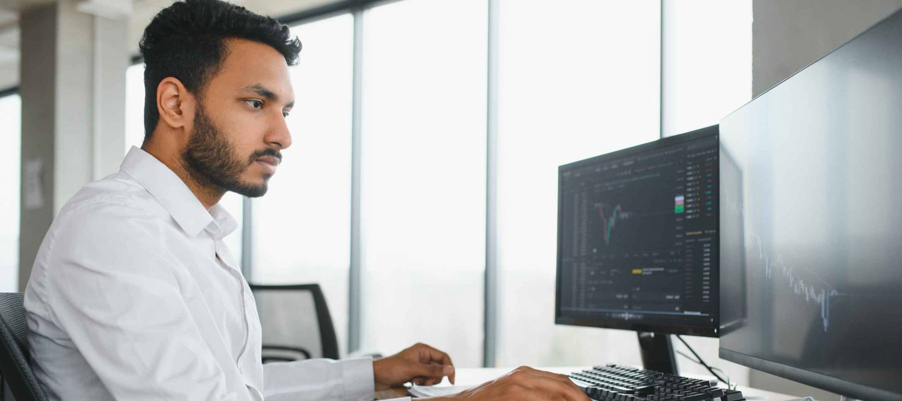 Young indian business man trader looking at computer screen with trading charts reflecting in eyeglasses watching stock trading market financial data growth concept, close up