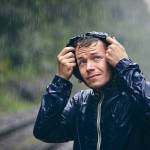 Trip in bad weather. Portrait of young man in drenched jacket in heavy rain.
