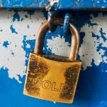 deadbolt lock  with the word gold embossed on it keeps a blue metal bin closed
