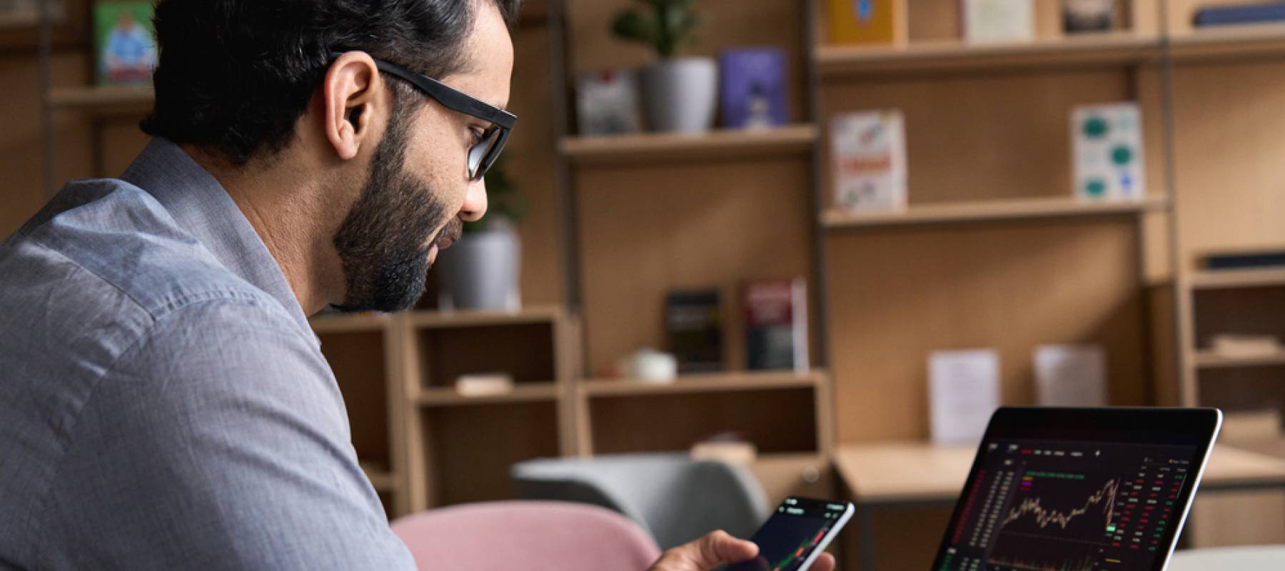 man in home office looking at investments on laptop and phone