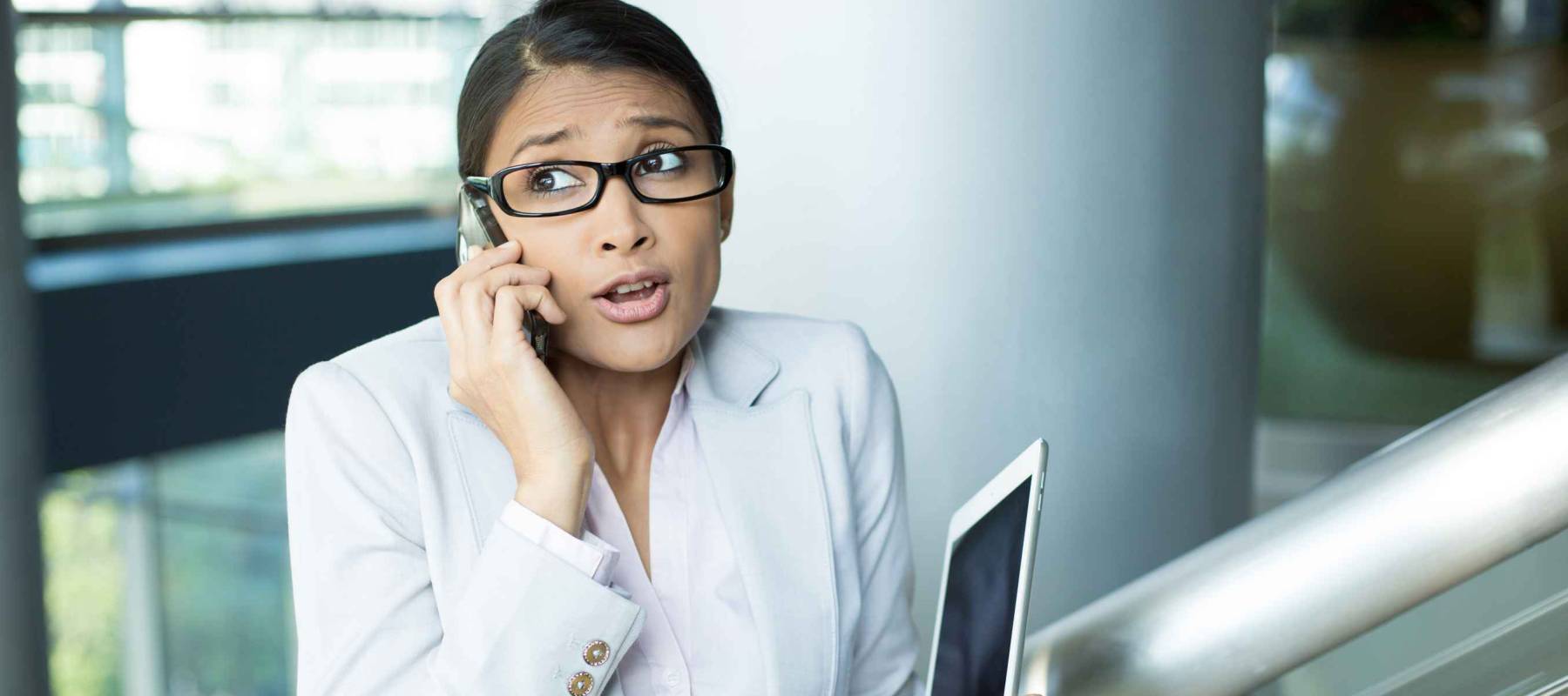 Closeup portrait of pretty busy woman in gray suit and pink shirt holding phone and tablet, sorry and apologizing for her mistakes, caught red-handed, isolated indoors office background