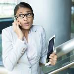 Closeup portrait of pretty busy woman in gray suit and pink shirt holding phone and tablet, sorry and apologizing for her mistakes, caught red-handed, isolated indoors office background