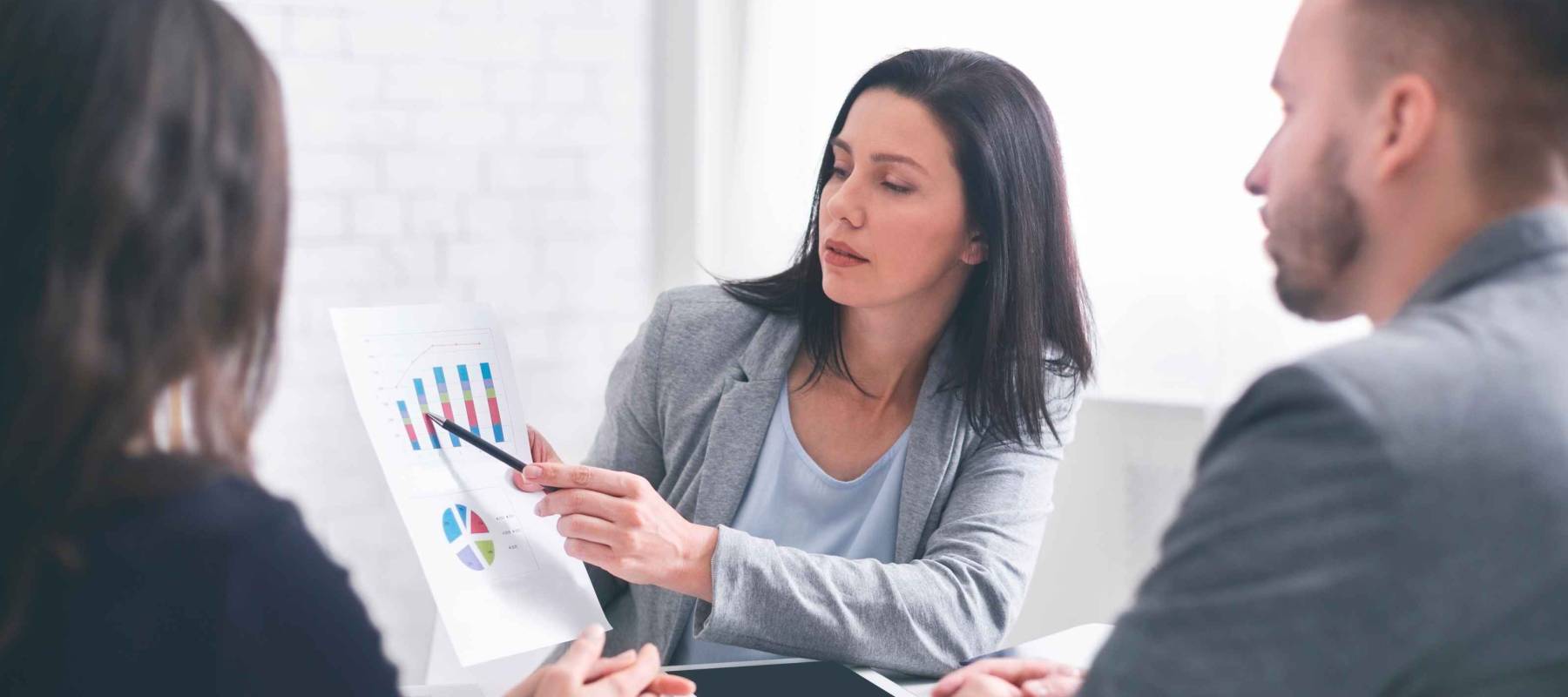 Professional woman broker giving presentation to young couple in her office, showing graphs to explain information to them